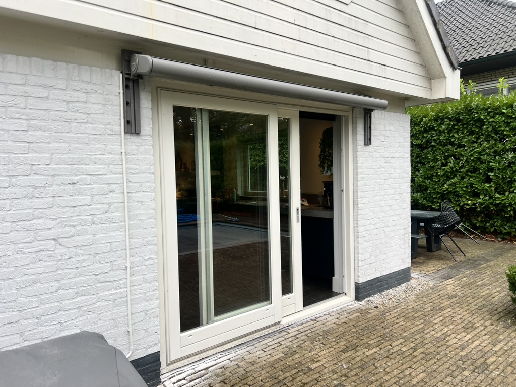 Screen gemonteerd boven een schuifpui in een witte bakstenen gevel